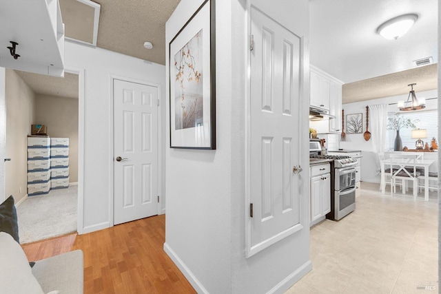 hallway with light wood-style floors, visible vents, baseboards, and a textured ceiling