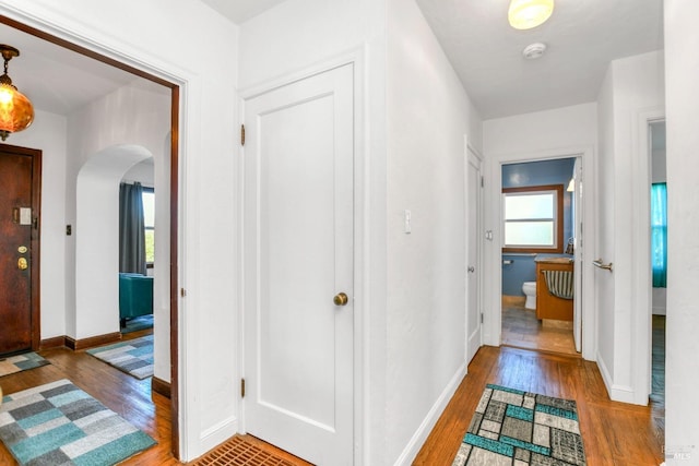 corridor with baseboards, arched walkways, and wood finished floors