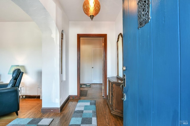 foyer entrance with baseboards, arched walkways, and dark wood-type flooring