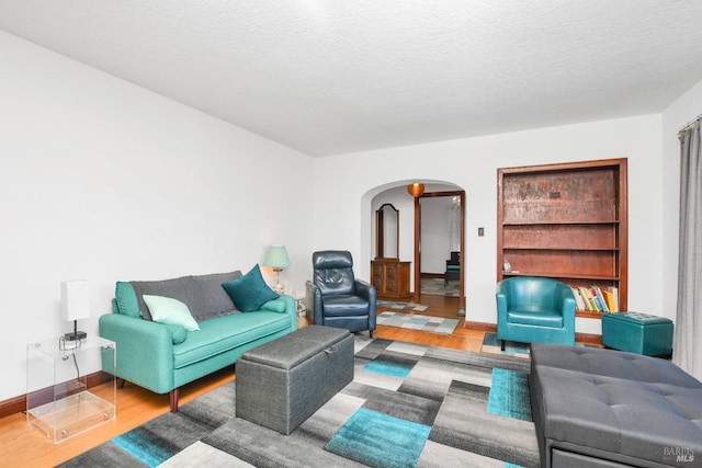 living room featuring baseboards, arched walkways, a textured ceiling, and wood finished floors