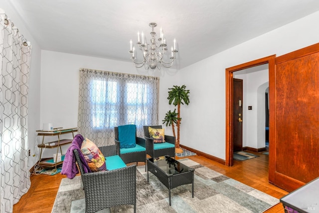 sitting room with an inviting chandelier, wood finished floors, arched walkways, and baseboards