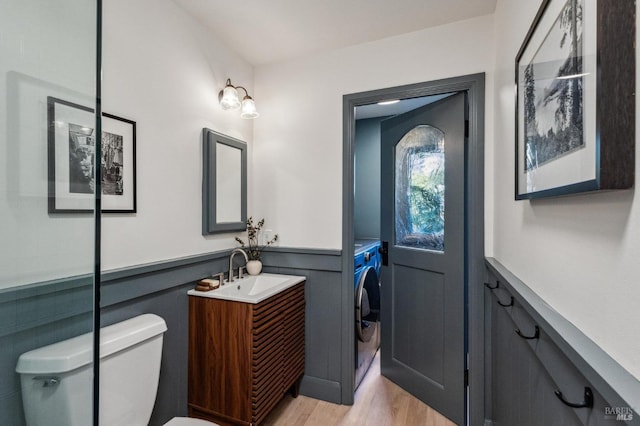 bathroom featuring vanity, wood finished floors, wainscoting, washer and dryer, and toilet