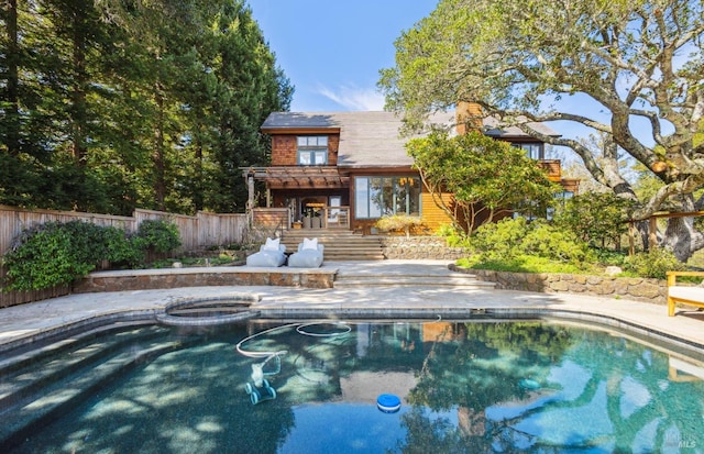 rear view of property featuring a pool with connected hot tub, a patio, and fence