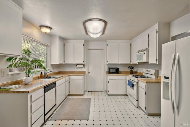 kitchen with a sink, white appliances, light floors, and white cabinets