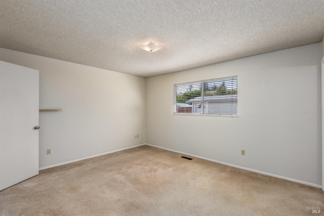 empty room featuring light carpet, visible vents, a textured ceiling, and baseboards