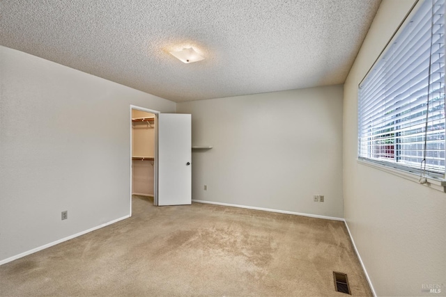 unfurnished bedroom featuring a walk in closet, visible vents, a textured ceiling, baseboards, and light colored carpet