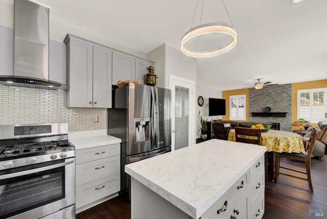 kitchen with a fireplace, dark wood-style flooring, stainless steel appliances, wall chimney range hood, and tasteful backsplash