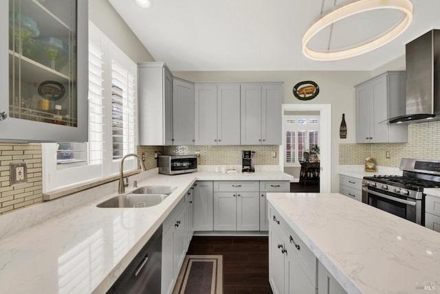 kitchen with light stone counters, a sink, dark wood-type flooring, appliances with stainless steel finishes, and wall chimney range hood