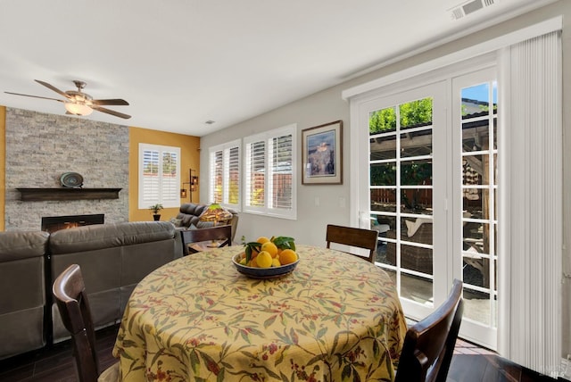 dining space with a stone fireplace, a ceiling fan, and visible vents