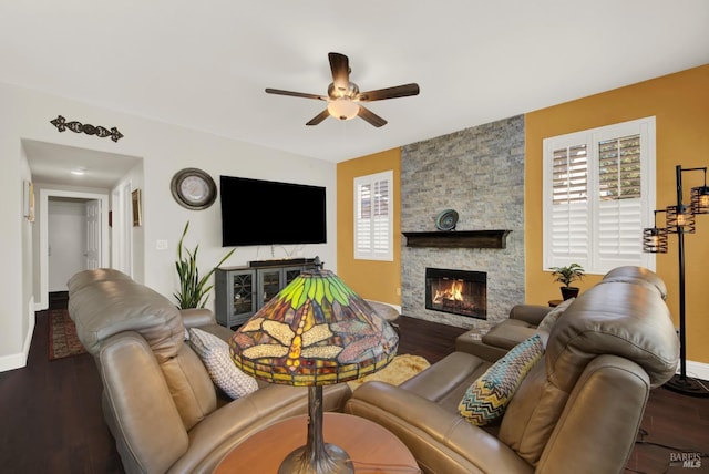 living room featuring baseboards, a stone fireplace, wood finished floors, and a ceiling fan