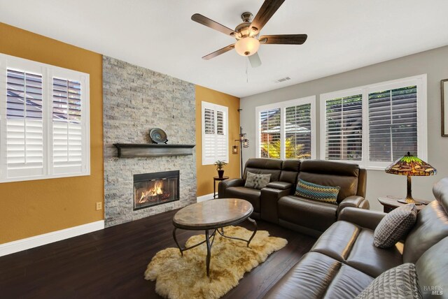 living room featuring visible vents, baseboards, ceiling fan, a fireplace, and wood finished floors