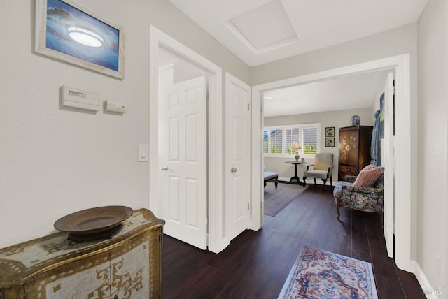 hall with attic access, baseboards, and dark wood-type flooring