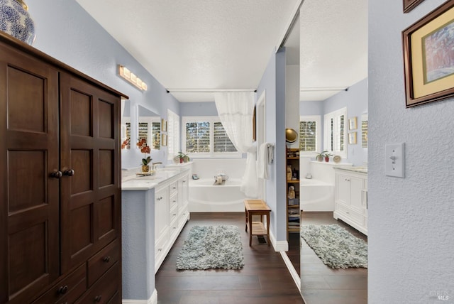 bathroom featuring a garden tub, two vanities, a textured ceiling, wood finished floors, and a textured wall