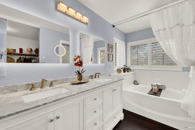 bathroom featuring double vanity, wood finished floors, a garden tub, and a sink