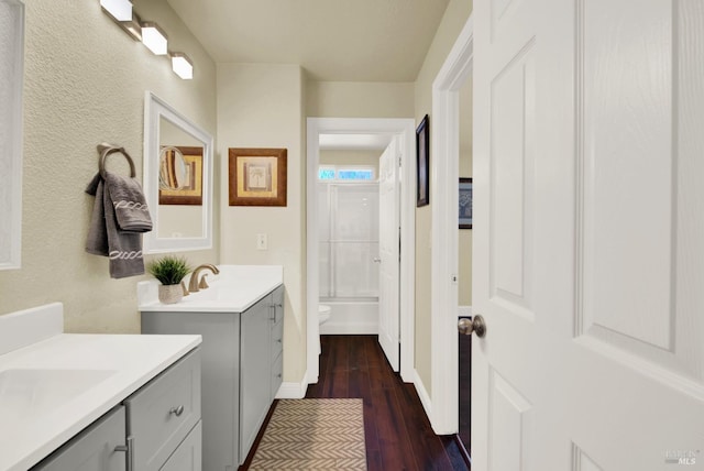 full bath featuring toilet, two vanities, wood finished floors, shower / bath combination, and baseboards