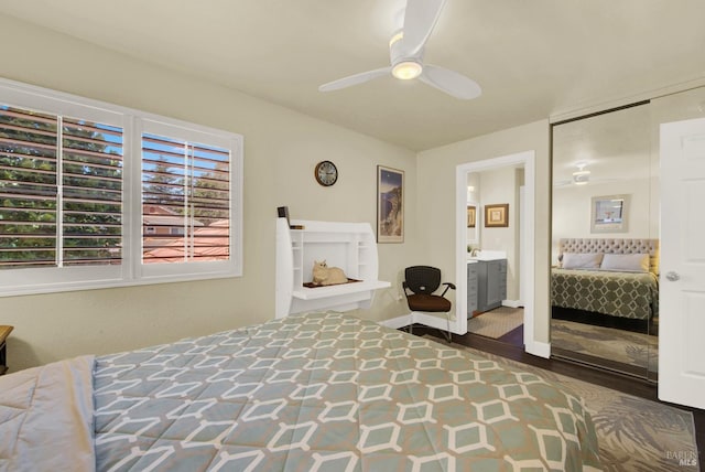 bedroom with wood finished floors, baseboards, ensuite bath, a fireplace, and ceiling fan