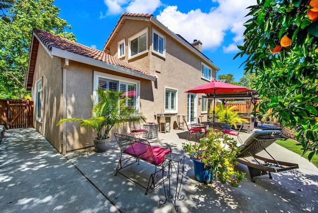 rear view of property featuring stucco siding, a patio, fence, a chimney, and a tiled roof