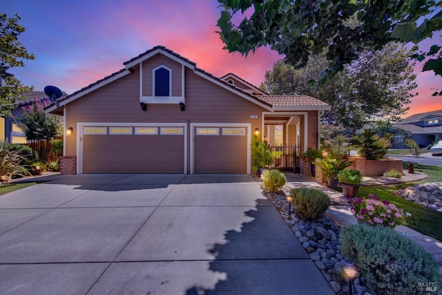 view of front of home featuring driveway, fence, a garage, brick siding, and a tiled roof