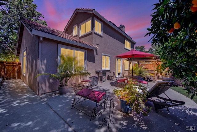 back of property with outdoor dining space, fence, a chimney, stucco siding, and a patio area