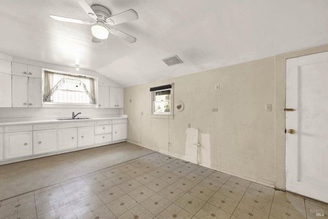 kitchen with light countertops, lofted ceiling, white cabinetry, a ceiling fan, and a sink