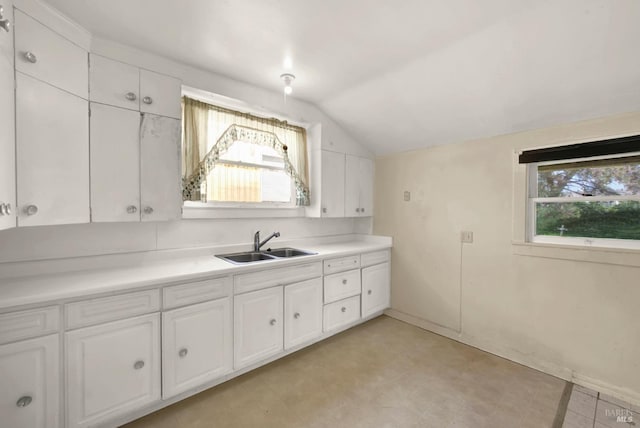 kitchen featuring white cabinets, light countertops, lofted ceiling, and a sink