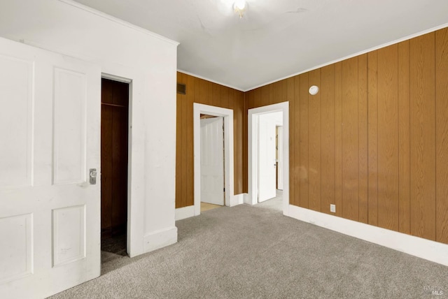 unfurnished bedroom featuring baseboards, wood walls, carpet flooring, and crown molding