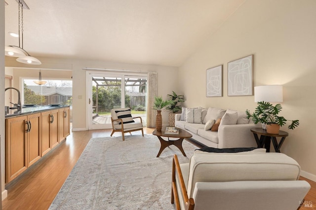 living room featuring baseboards, vaulted ceiling, and light wood-style flooring