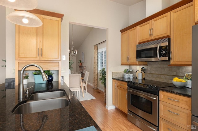 kitchen with stainless steel appliances, a sink, light wood-type flooring, dark stone counters, and tasteful backsplash