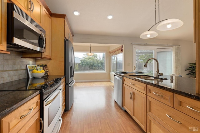 kitchen with a sink, hanging light fixtures, light wood finished floors, backsplash, and appliances with stainless steel finishes