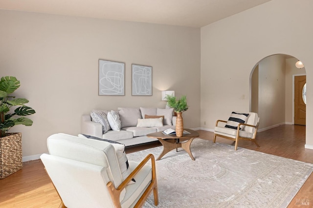 living area featuring arched walkways, light wood finished floors, and baseboards