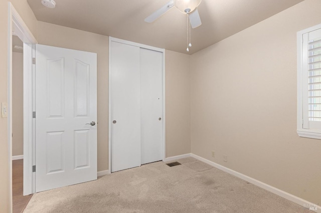 unfurnished bedroom featuring visible vents, baseboards, light colored carpet, a ceiling fan, and a closet