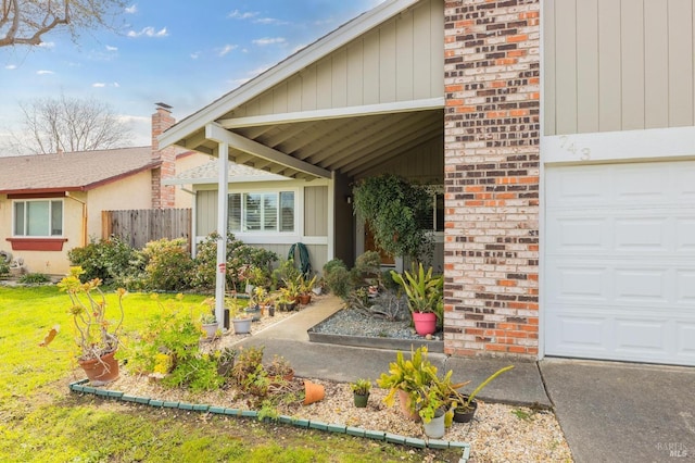 entrance to property featuring a chimney, fence, brick siding, a garage, and a lawn