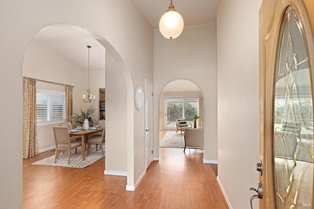 entrance foyer featuring a chandelier, a high ceiling, arched walkways, light wood-style flooring, and baseboards
