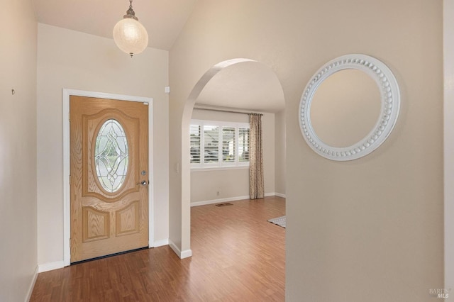entrance foyer featuring arched walkways, vaulted ceiling, visible vents, baseboards, and wood finished floors