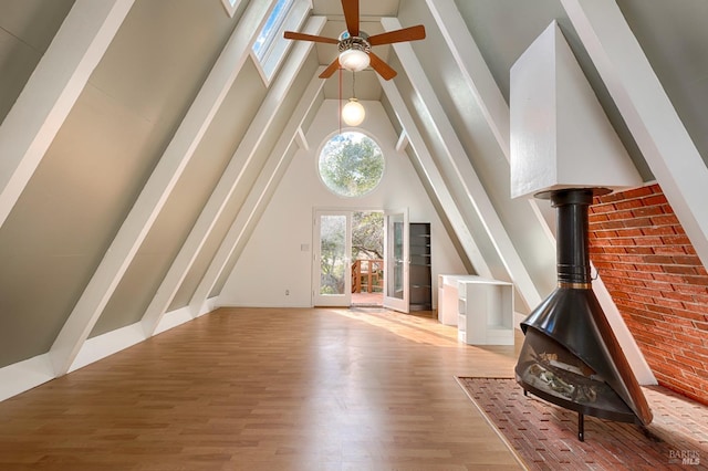 additional living space with a ceiling fan, a wood stove, wood finished floors, and high vaulted ceiling