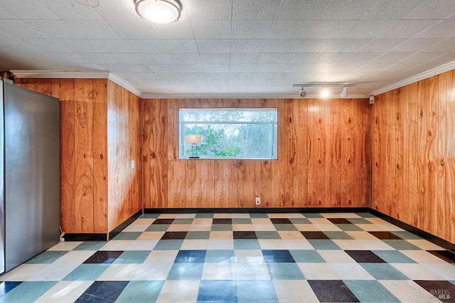 unfurnished room featuring tile patterned floors, baseboards, wood walls, and crown molding