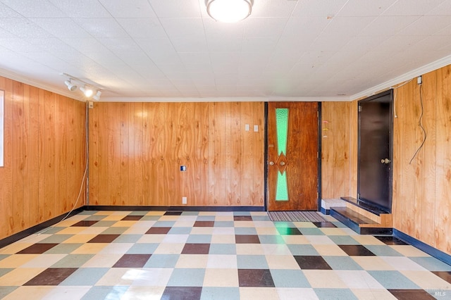 spare room featuring tile patterned floors, baseboards, wood walls, and track lighting