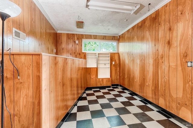 spare room featuring wooden walls, visible vents, ornamental molding, a textured ceiling, and tile patterned floors