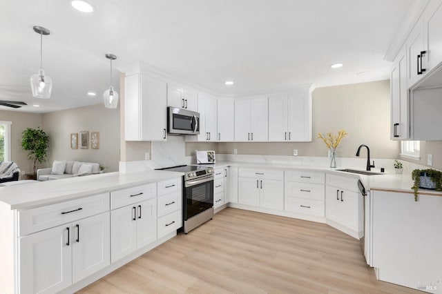 kitchen featuring light wood finished floors, open floor plan, appliances with stainless steel finishes, a peninsula, and a sink