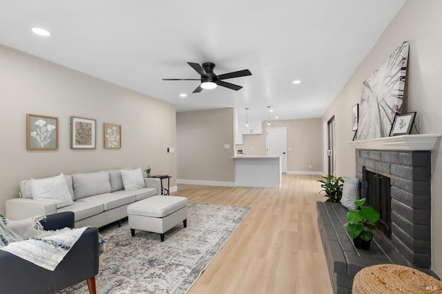 living room with ceiling fan, baseboards, recessed lighting, a fireplace, and light wood-style floors