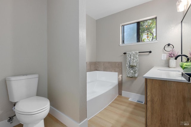 bathroom with vanity, wood finished floors, baseboards, a garden tub, and toilet