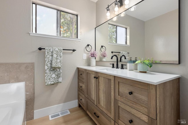 bathroom featuring vanity, wood finished floors, a tub to relax in, visible vents, and baseboards