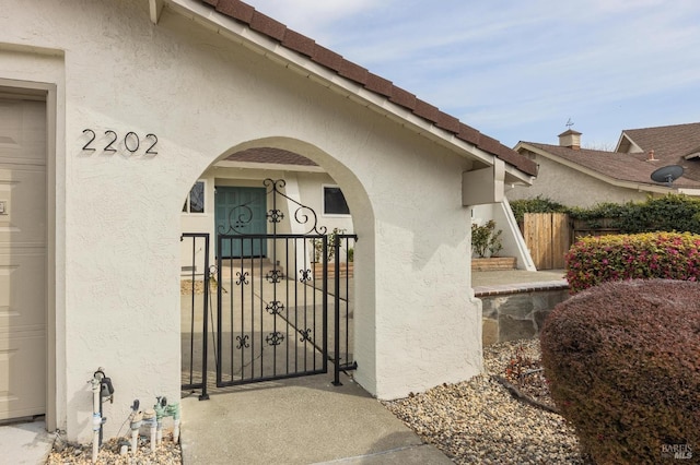 view of exterior entry featuring stucco siding, fence, a garage, and a gate