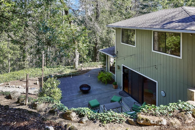 view of property exterior with a forest view, a patio area, and a shingled roof