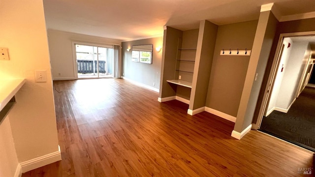 unfurnished living room with wood finished floors, baseboards, and ornamental molding