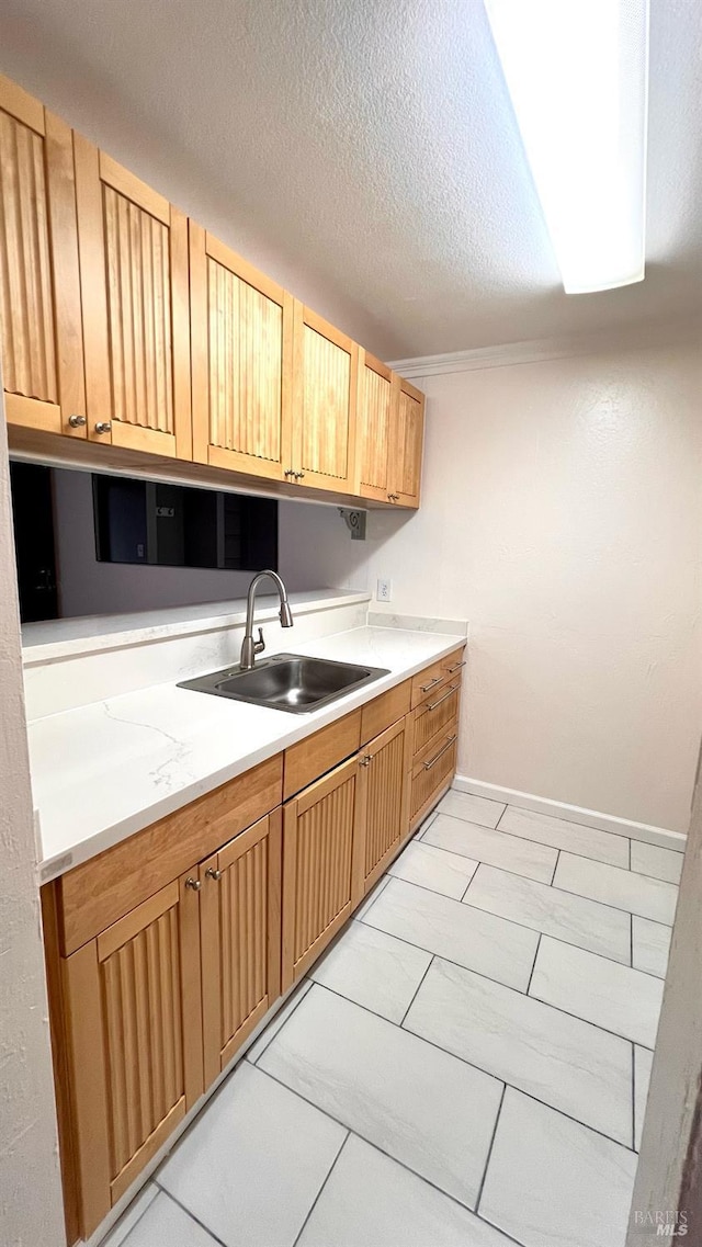 kitchen with light countertops, a textured ceiling, baseboards, and a sink