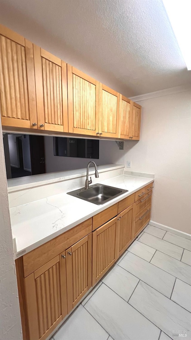 kitchen with baseboards, a sink, light countertops, a textured ceiling, and crown molding