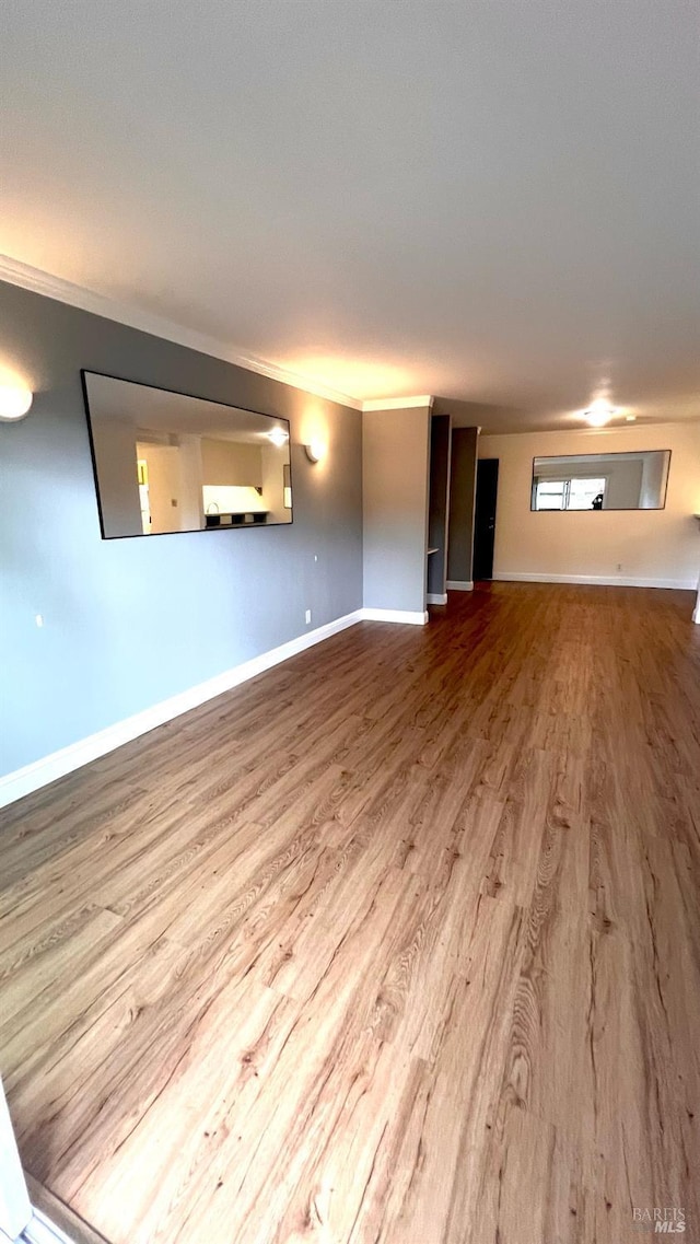 unfurnished living room with wood finished floors, baseboards, and ornamental molding