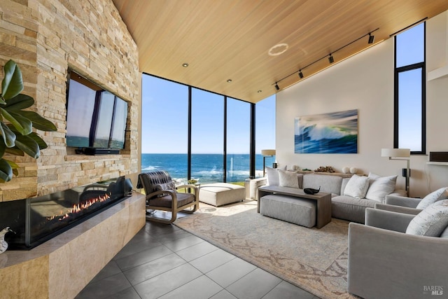 living room with rail lighting, tile patterned flooring, a wall of windows, wooden ceiling, and a stone fireplace