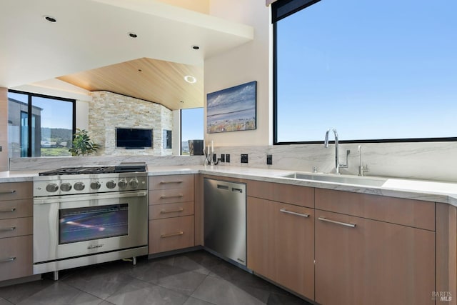 kitchen featuring a sink, backsplash, light stone countertops, light brown cabinetry, and appliances with stainless steel finishes